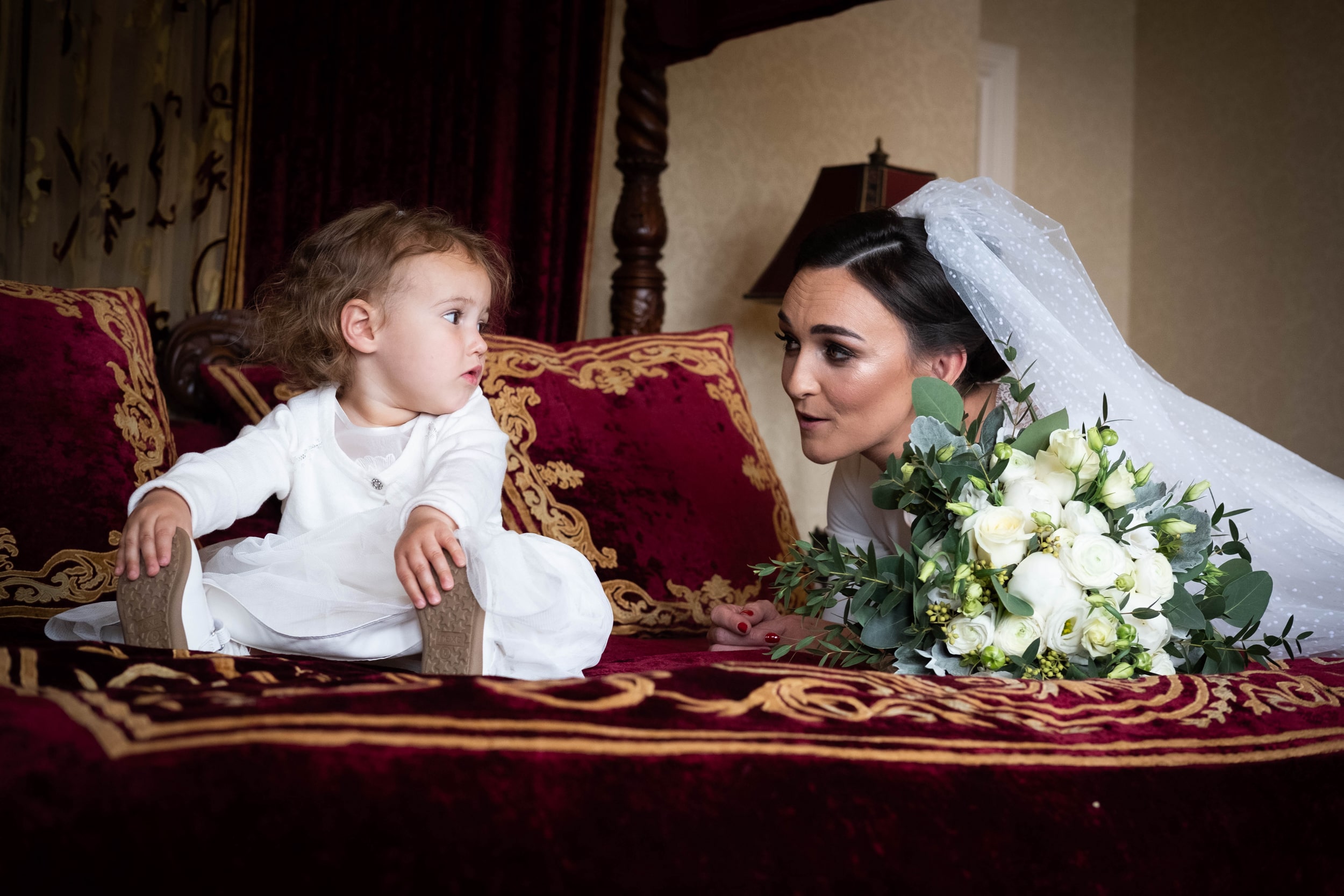 Bride leaning onto the bed, looking at The little flower girl in Kilronan Castle bridal suite