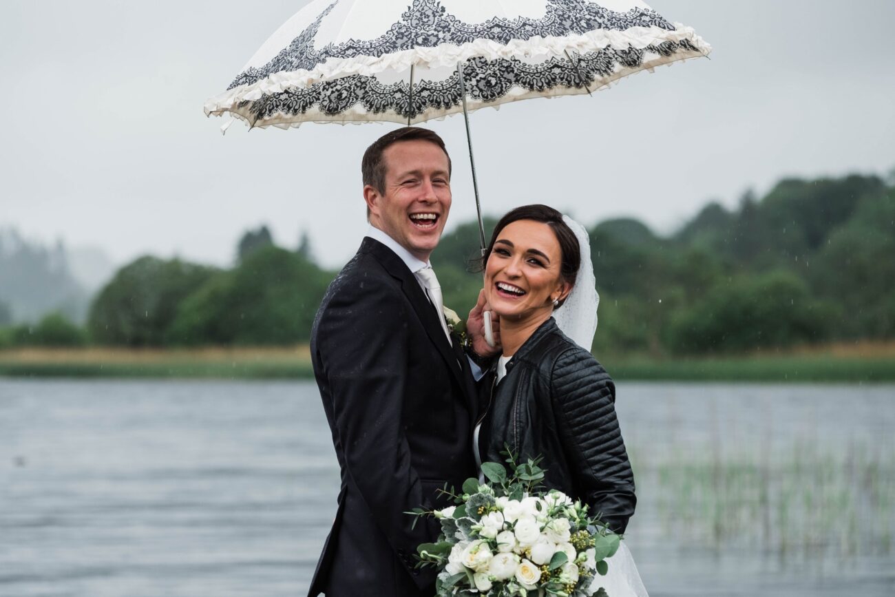 Bride and Groom standing under an unbrella in the rain at Kilronan Castle wedding