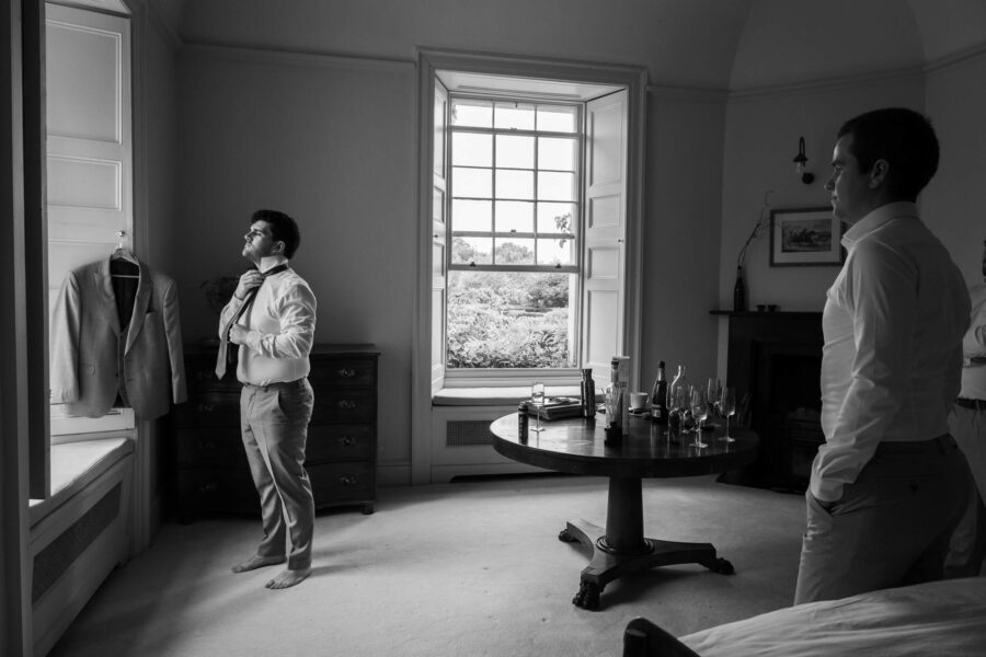 Groom doing his tie and looking out the window at Ballintubbert House and Gardens