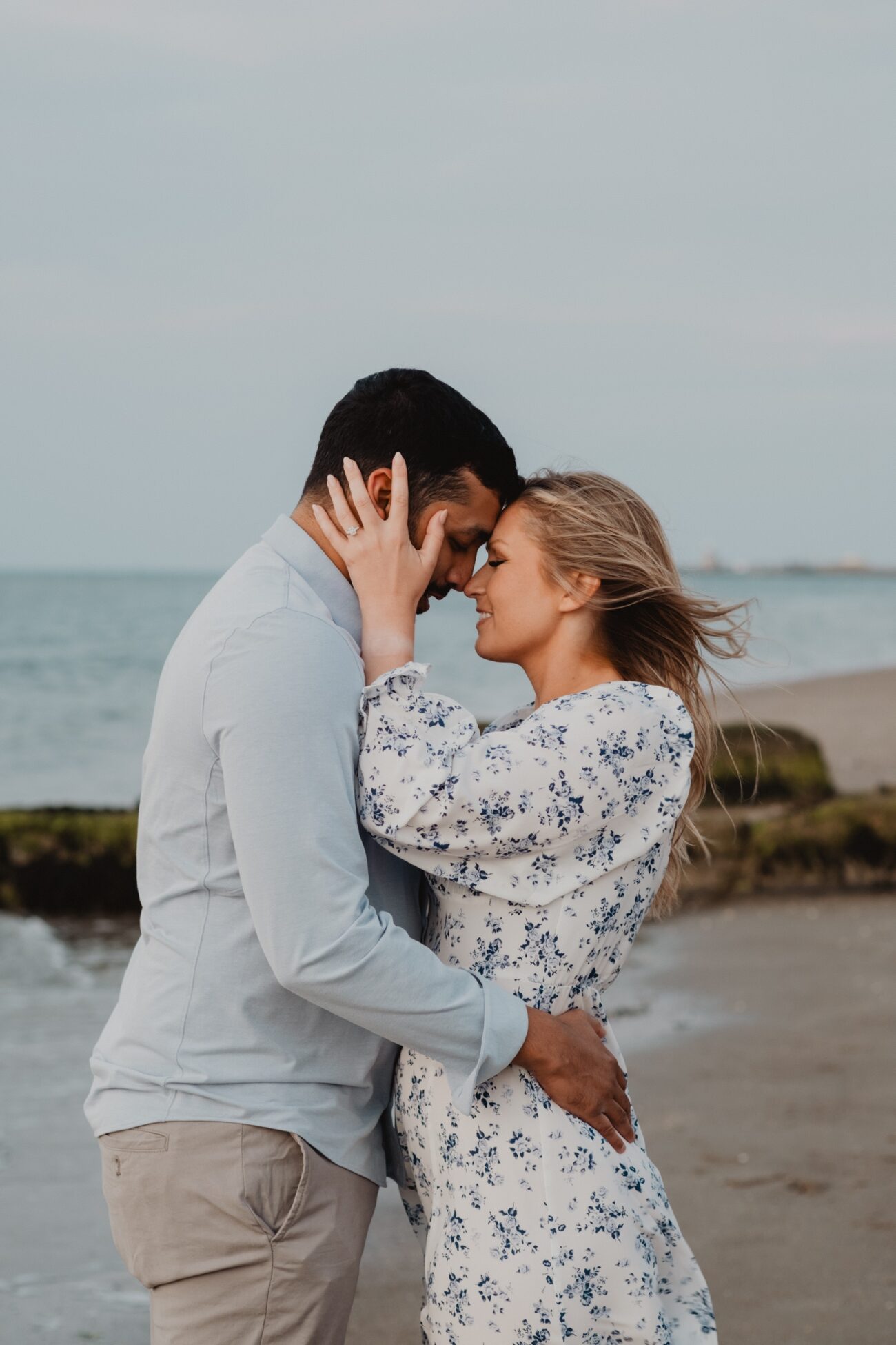 couples holding each other closely in the wind at Burrow Beach, Howth. Engagement photography Howth