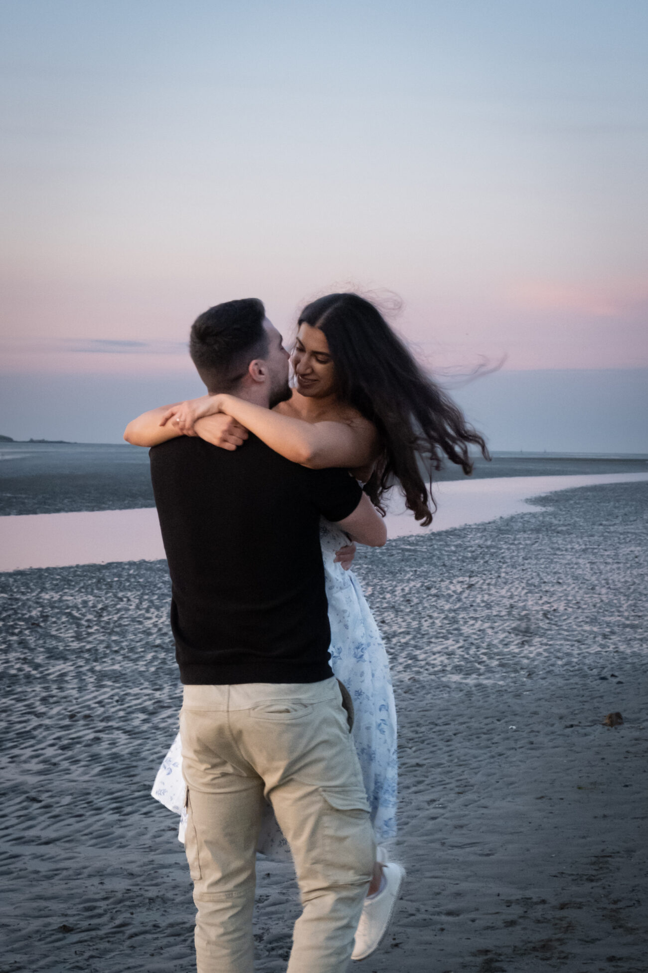 man lifting his girlfriend romantically on the beach in Burrow Beach