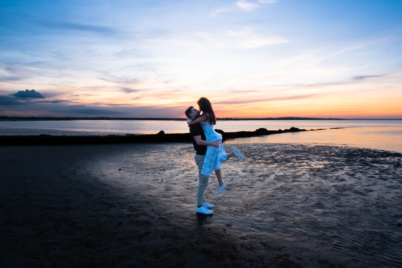 man lifting his girlfriend romantically on the beach in Burrow Beach