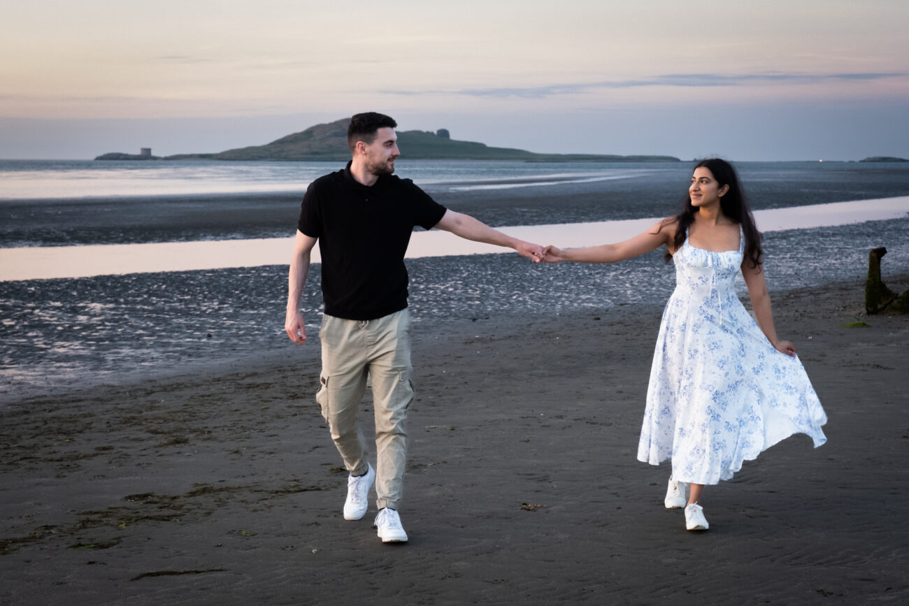 couple holding hands and walking on the beach in Burrow Beach Howth