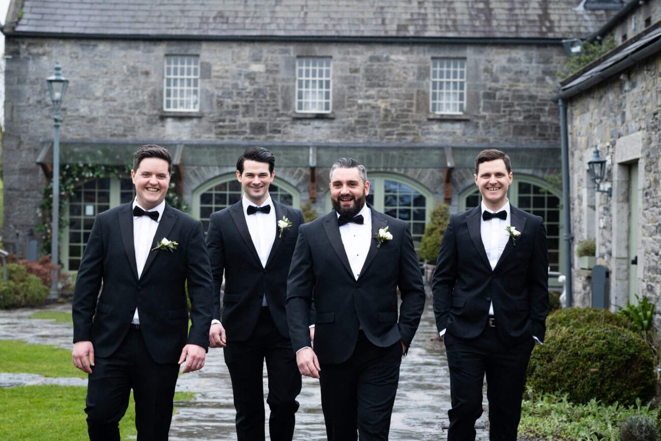 groomsmen walking towards the camera in the courtyard of Ballymagarvey Village