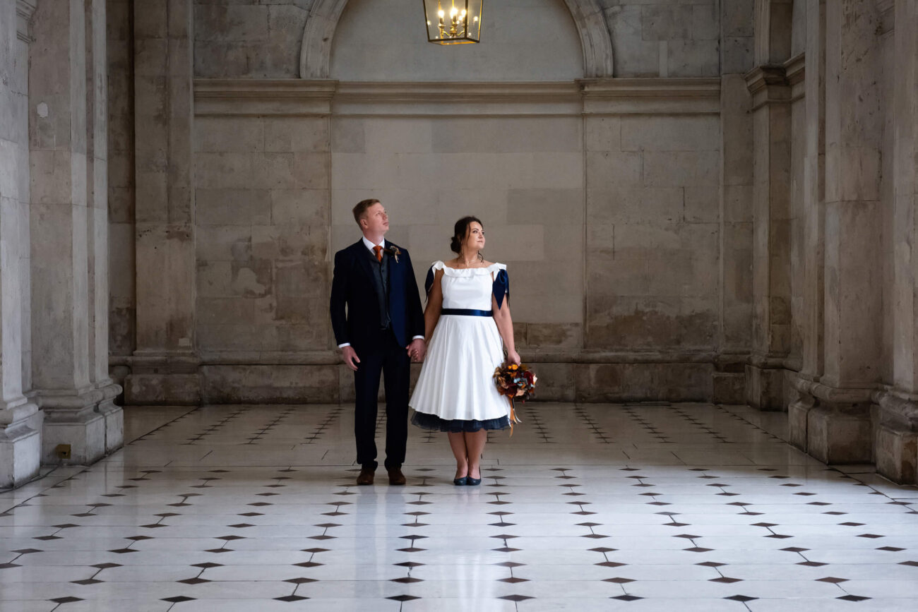 couple standing inside Dublin city hall holding hands and looking out the window.