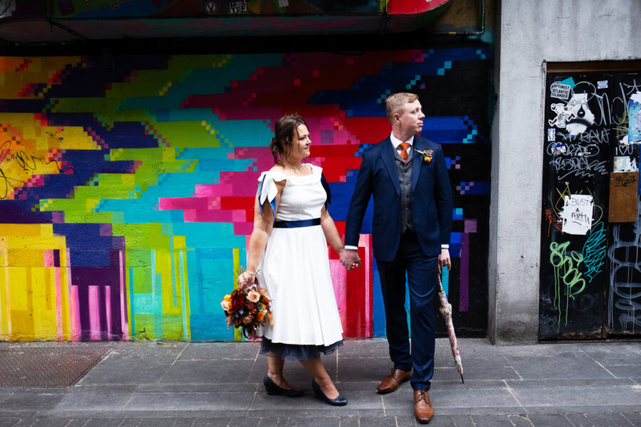 couple holding hands, standing in front of a graffiti wall