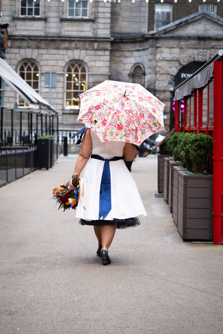 bride walking down the street in Dublin with pink umbrella