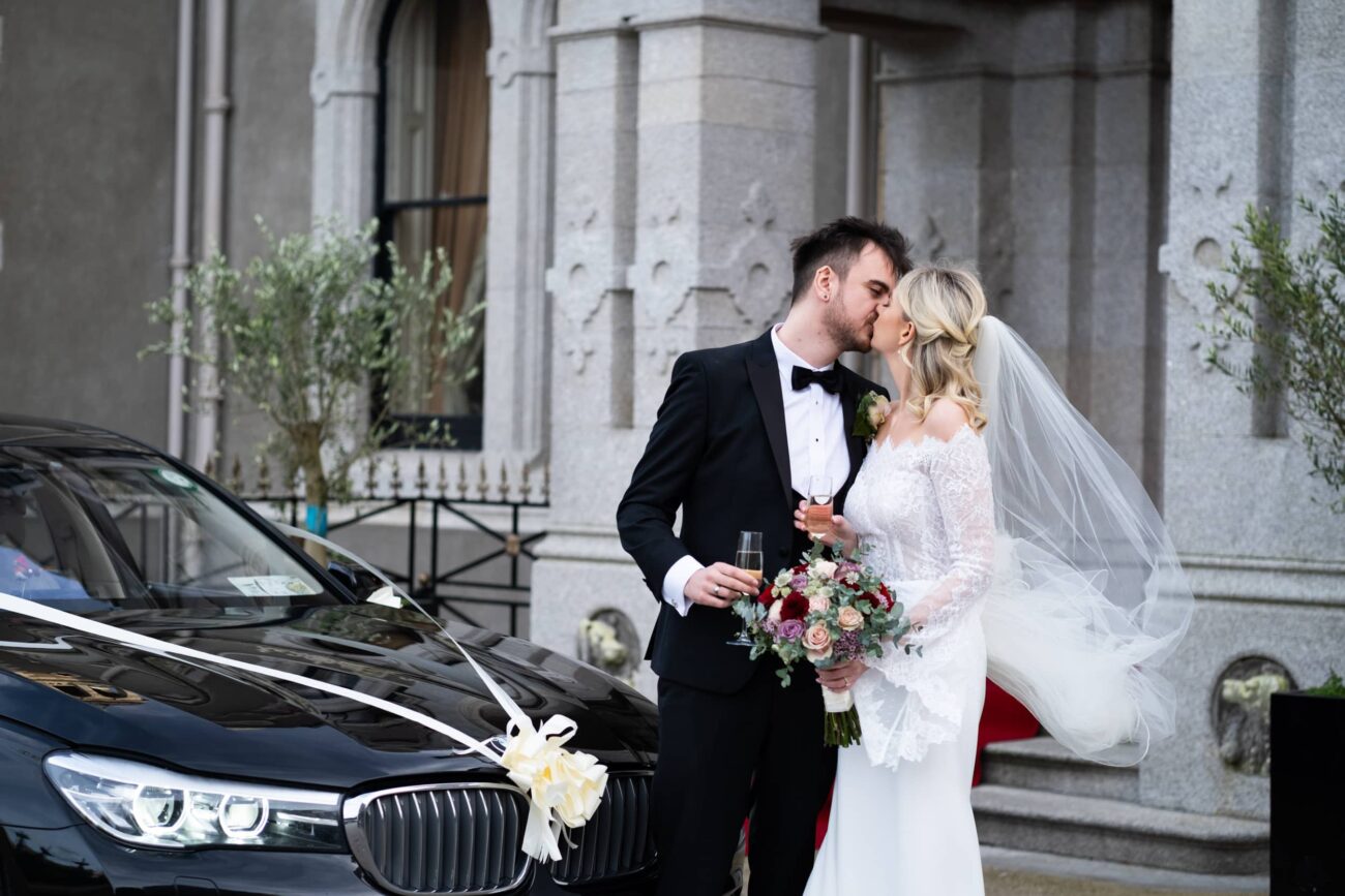 Bride and groom kissing next to the car at the front of Killashee Hotel