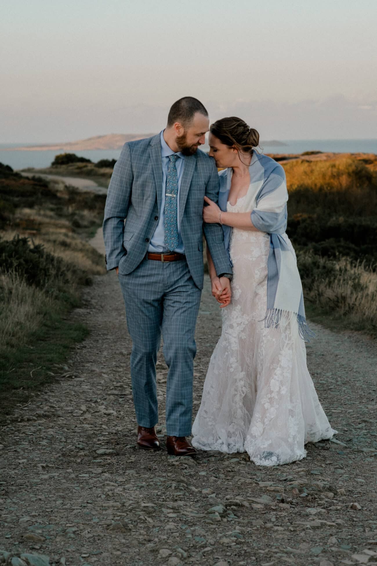 bride kissing her husbands shoulder as they walk in the landscape of Howth Summit. Elopement photography in Howth Summit