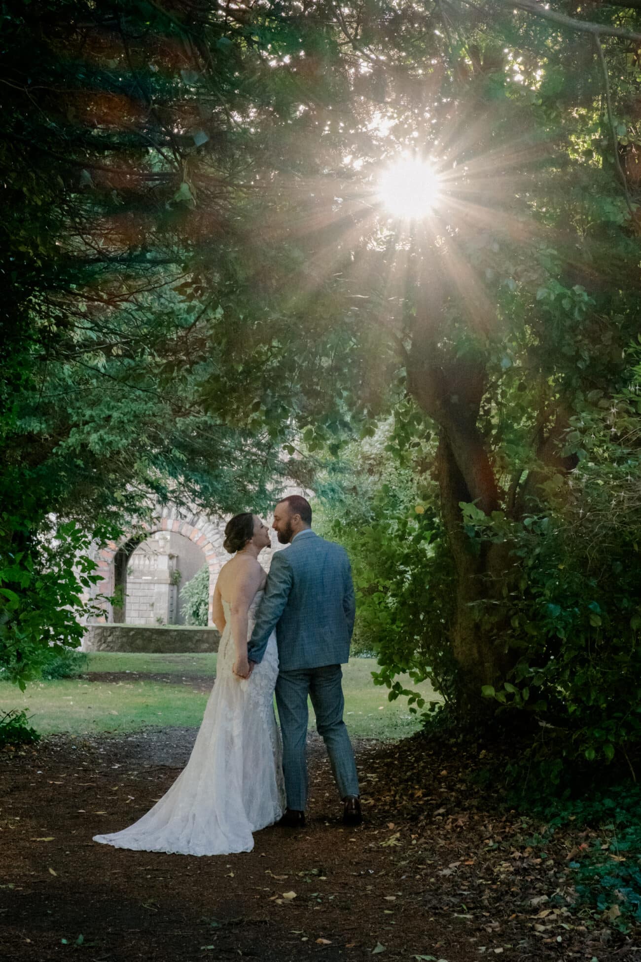 Couple holding hands and looking into each others eyes with the sunlight shining though the trees at Howth Castle