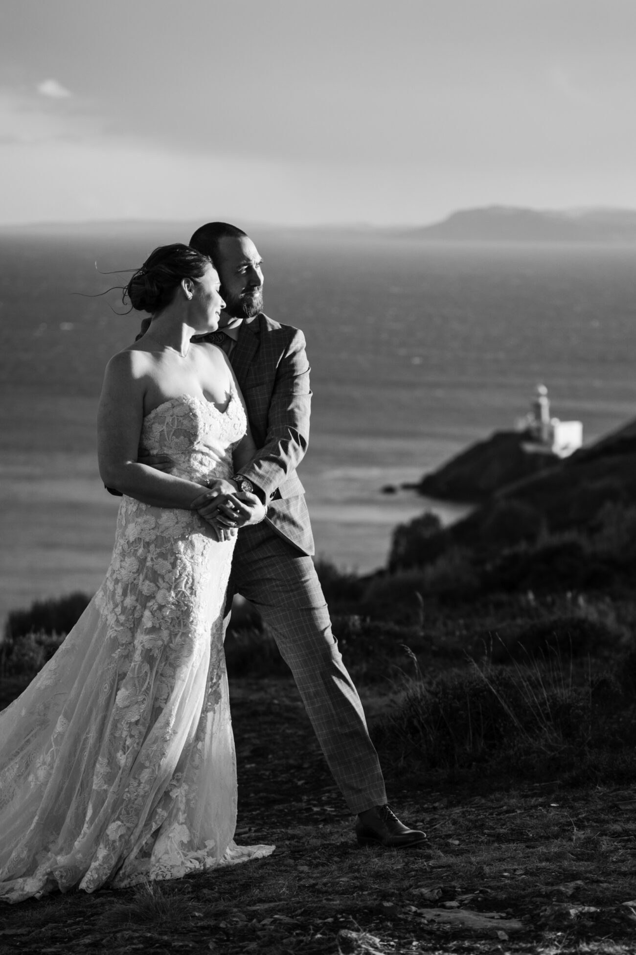 couple facing into the sunset with Howth lighthouse in the background. Couples photography in Howth