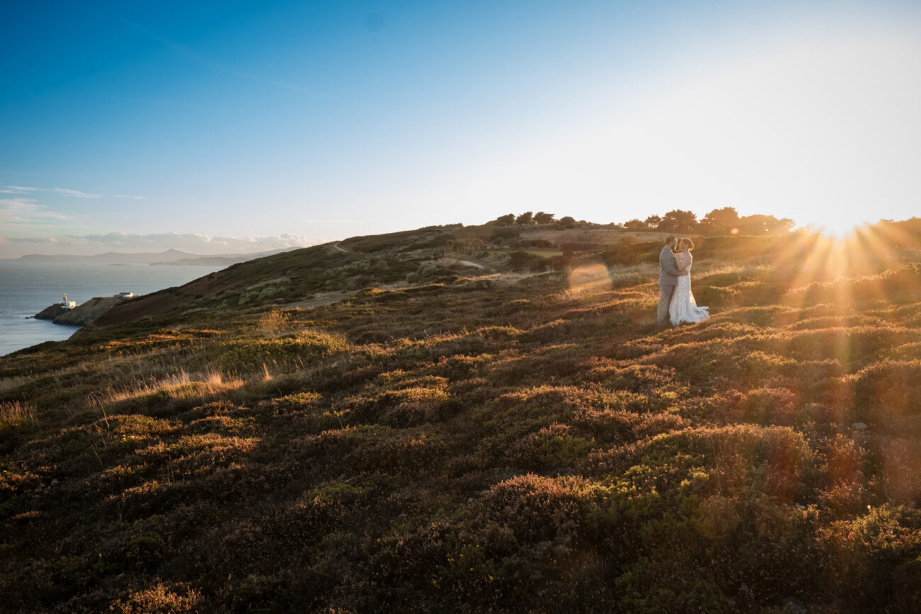 wide shot of couple standing in Howth Cliffs with sunset