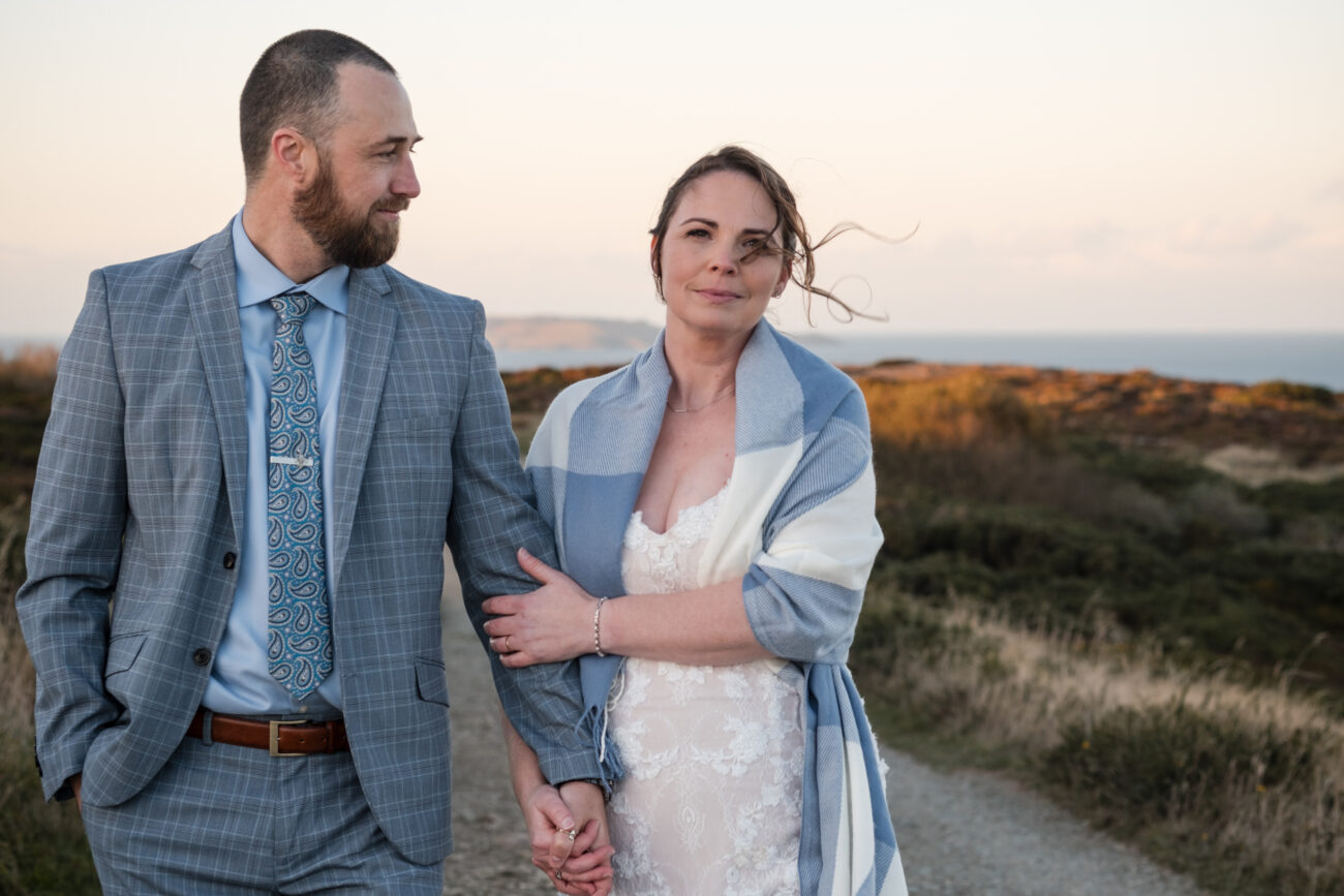 couple walking arm in arm in the Cliffs of Howth, groom looking loving at his bride as she stares at the camera