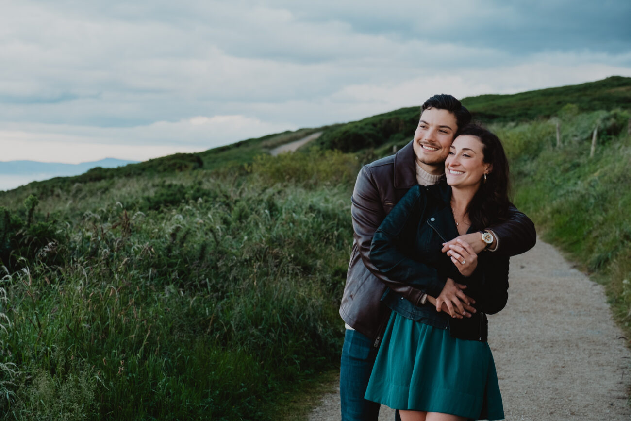 Couple hugging and looking into the distance on Howth Head. Secret proposal on Cliffs of Howth