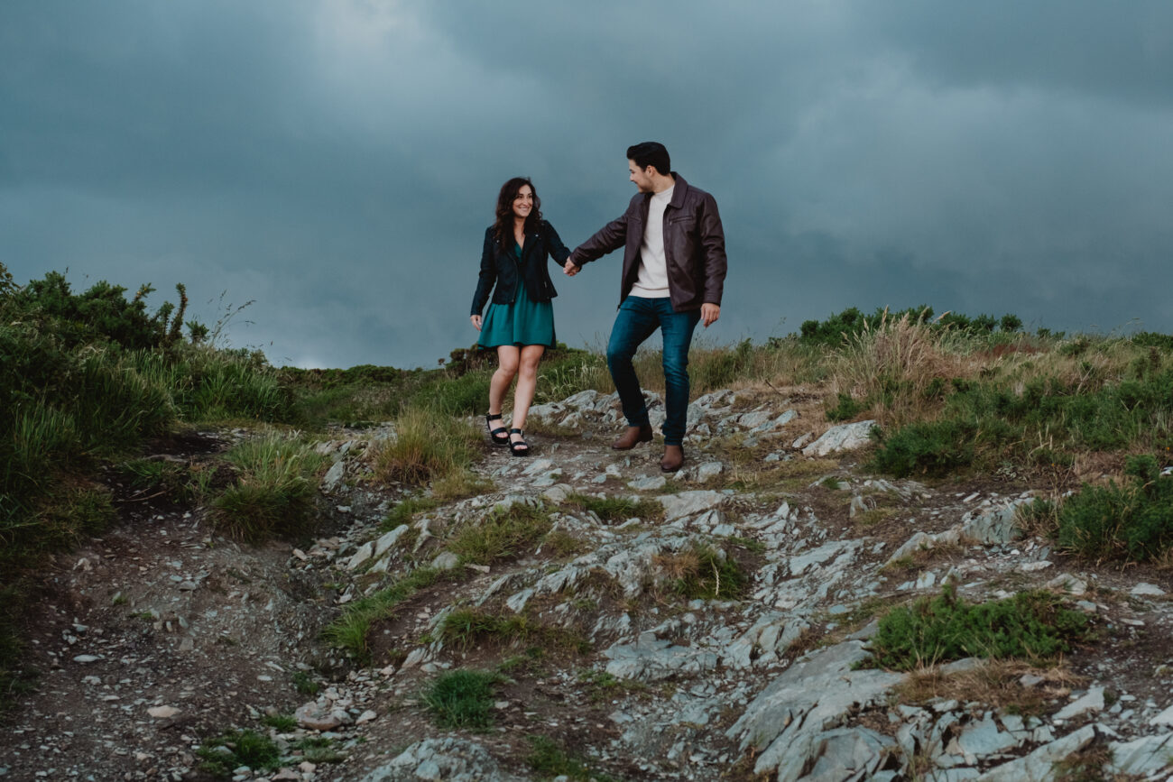 Couple down a rocky hill and holding hands on Howth Head. Secret proposal on Cliffs of Howth