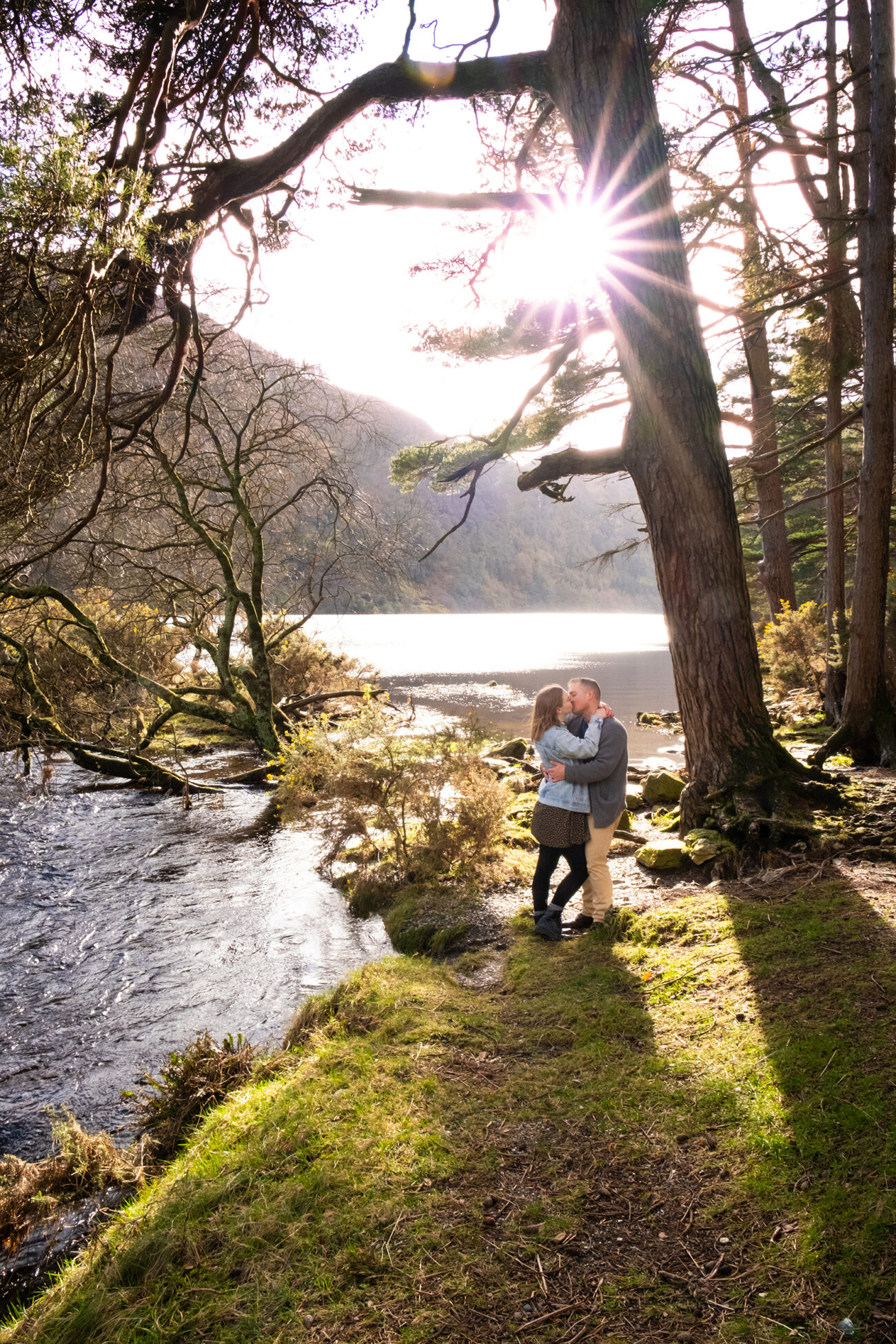 Couple kissing under the trees with the sunset at the upper lake in Glendalough