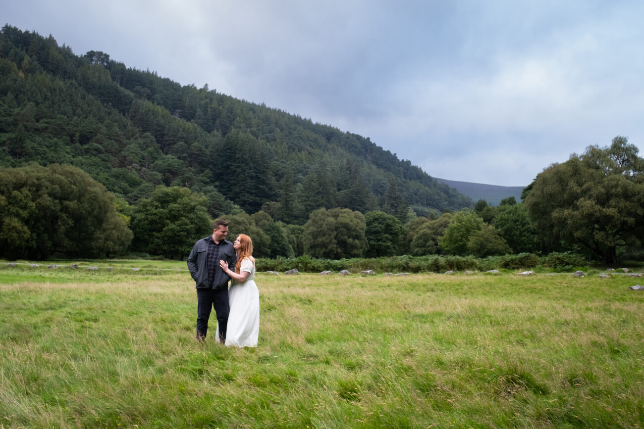 couple embracing during an engagement shoot in Glendalough. The green hills behind them