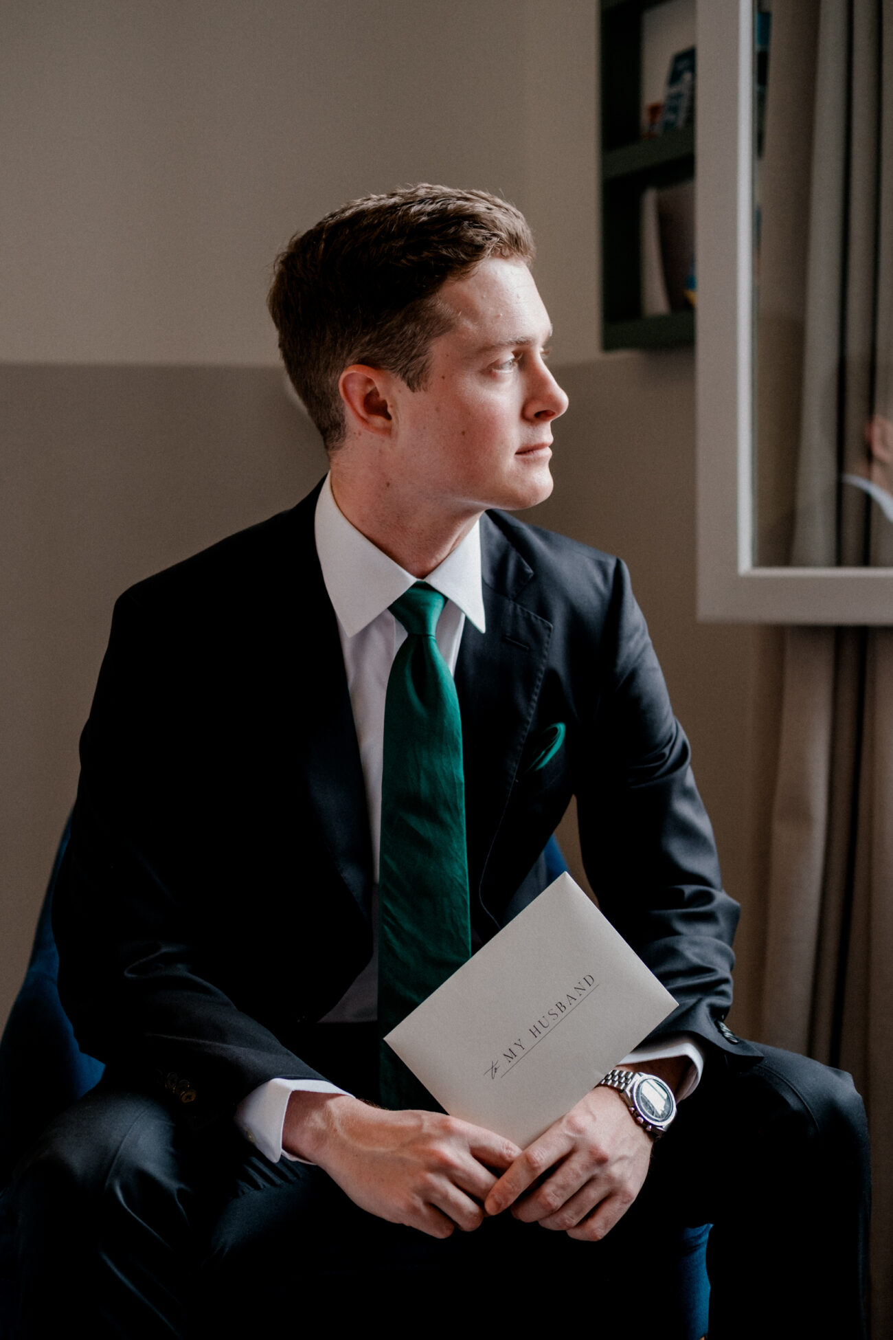 Groom holding his wedding letter and looking out the window. Dublin elopement