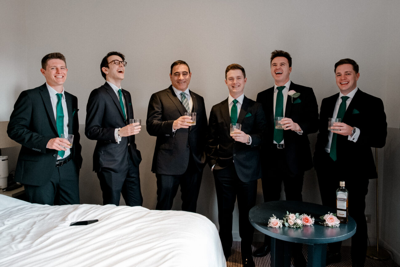 Groomsmen having a toast of whiskey and laughing during groom prep. Candid wedding photography
