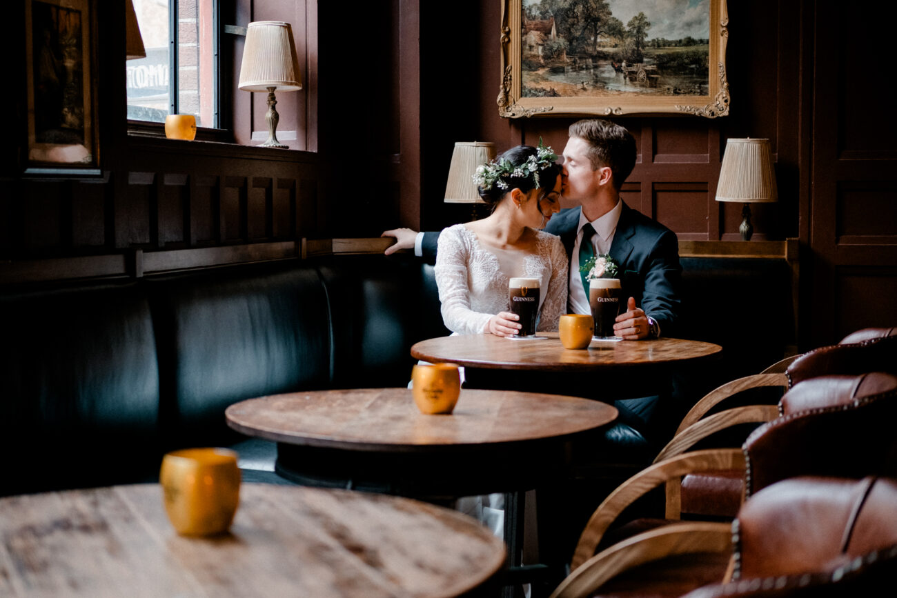 husband kissing wifes forhead whilst sitting in a quiet pub drinking Guinness at The Clarence Hotel, Canid wedding portrait, Clarence Hotel elopement