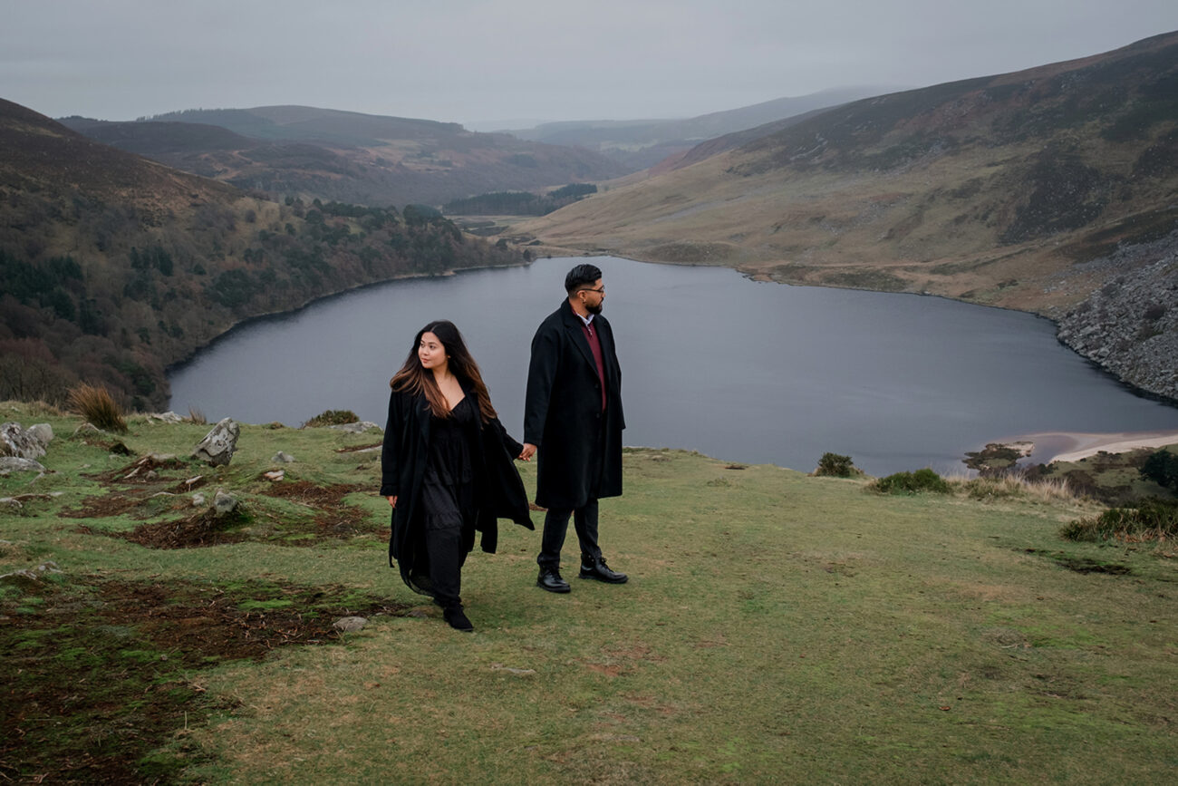 couple holding hands and looking into the distance at a secret proposal in Lough Tay